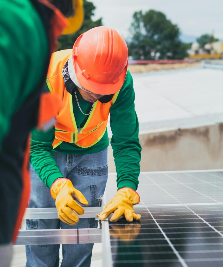 Worker in safety gear installing solar panels on a rooftop.